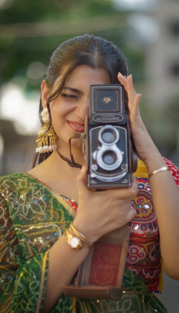 Still from the Chaniya Choli film: a woman in a mirror-work chaniya choli and green dupatta looking through a vintage twin-lens camera